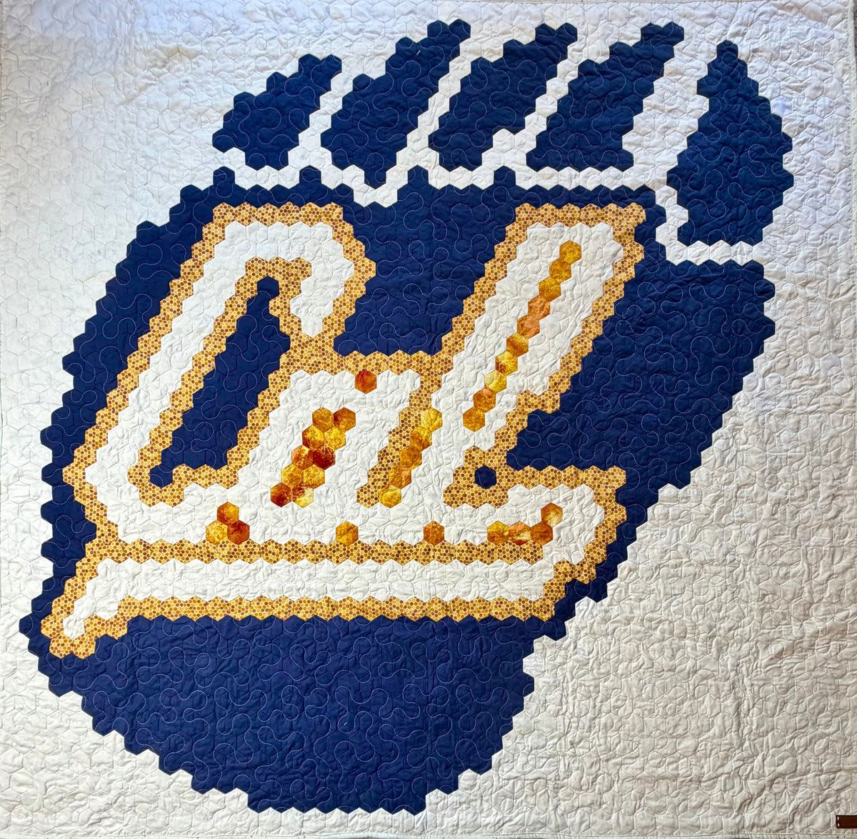A California State themed handmade hexagon quilt patchwork design featuring a large blue and white stylized 'Cal' monogram with amber-colored glass bead accents, set against a white quilted background.
